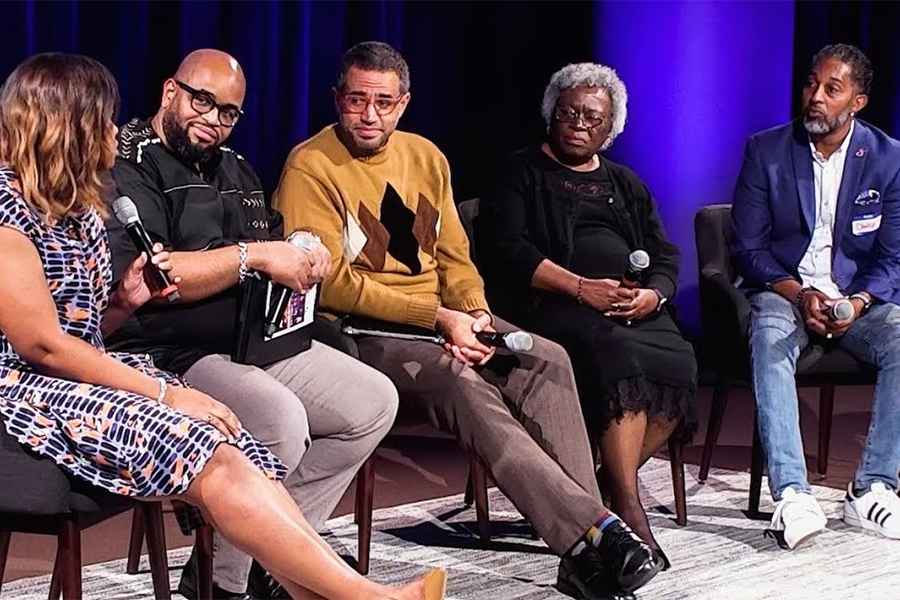 A group of Black professionals sitting on stage participating in a question and answer session.