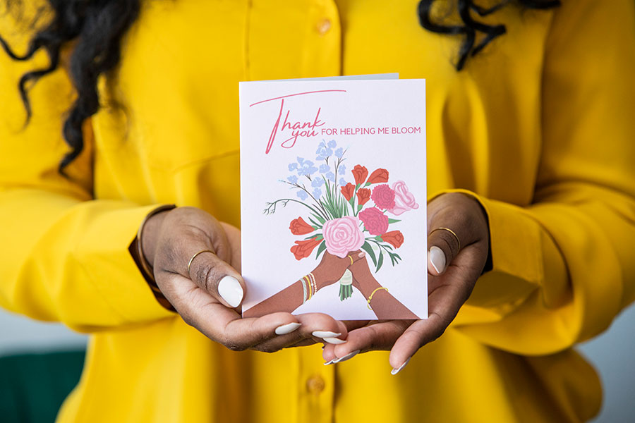 Asha Banks wearing bright yellow suit holding CheerNotes greeting card toward camera