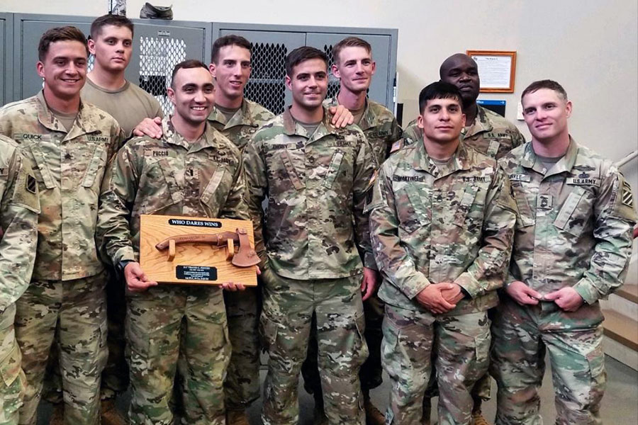 travis and military colleagues in camouflage uniforms holding a winning plaque and smiling at camera 