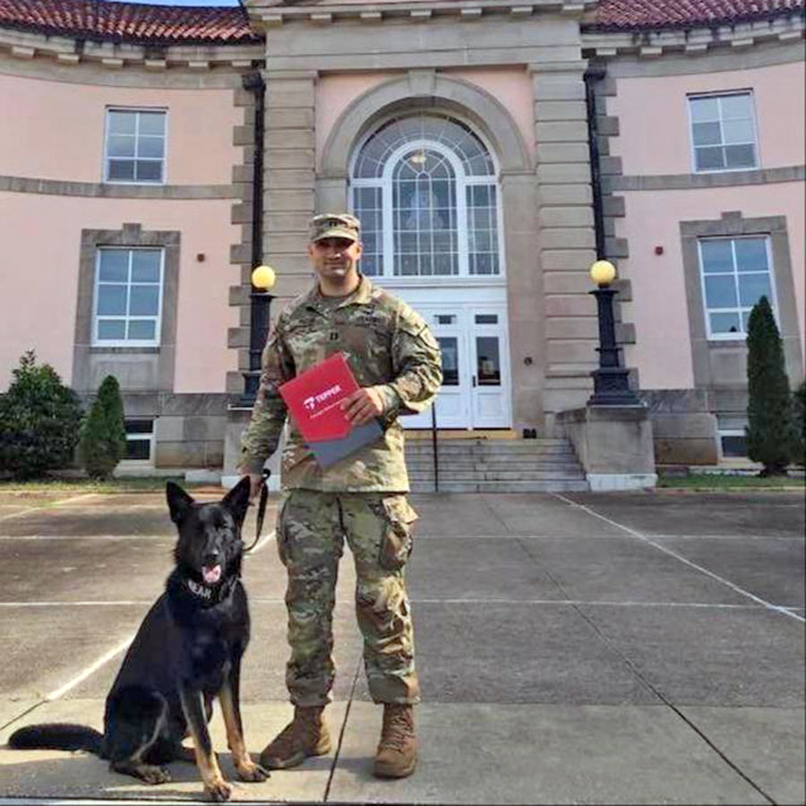 travis with military service dog standing in front of Carnegie Mellon's campus holding a red welcome to Tepper folder
