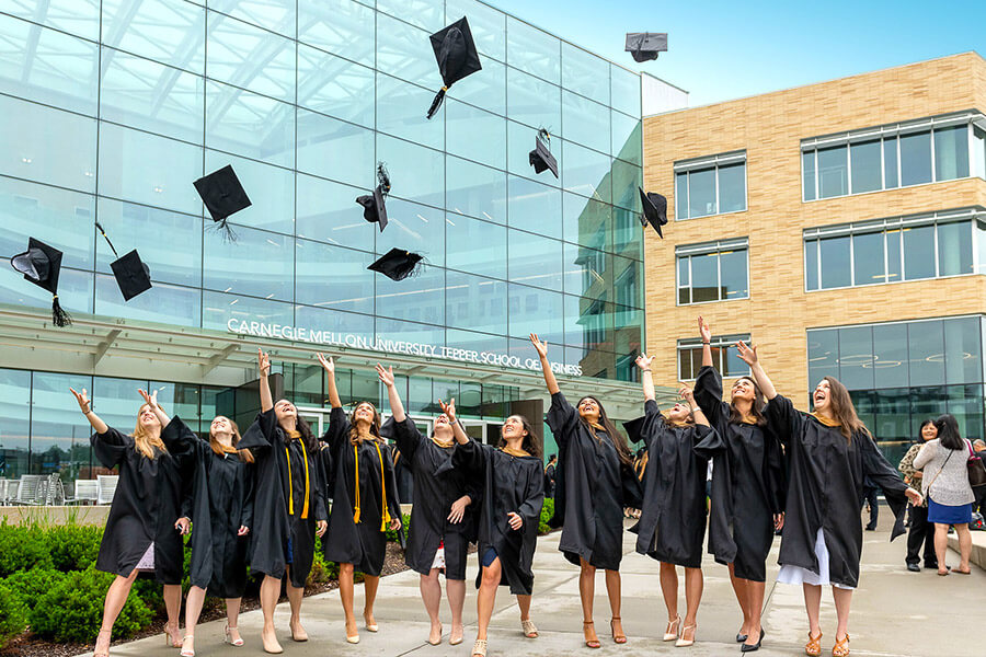 Group of female students throw their graduation caps in the air in front of the Tepper building.