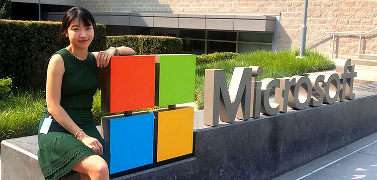 MBA Inno Zhang sitting next to a Microsoft sign at her internship.