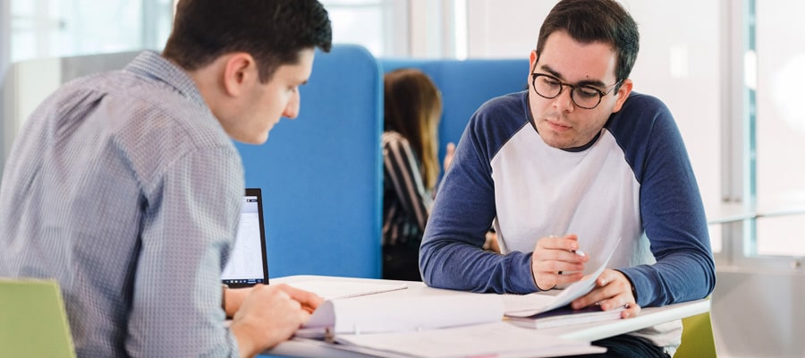 photo of two male doctoral students conversing over paperwork