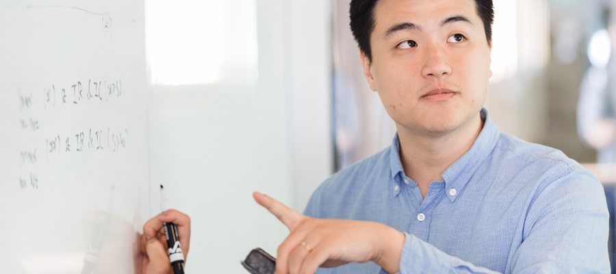 photo of male phd student wearing blue shirt and writing on white board wall