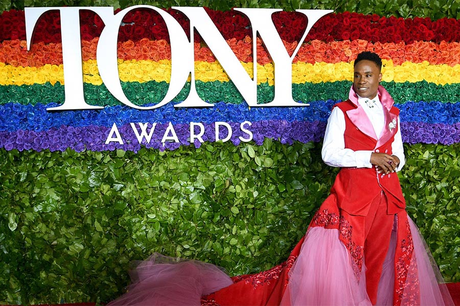 Photo of Billy Porter on the red carpet by the Tony Awards logo and rainbow rose display.