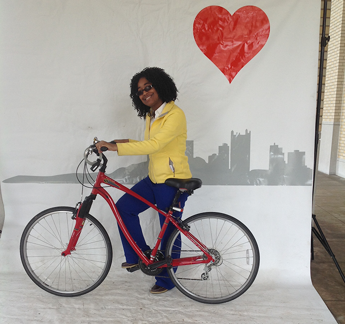 person standing with a bike, with drawing of Pittsburgh city skyline in the background