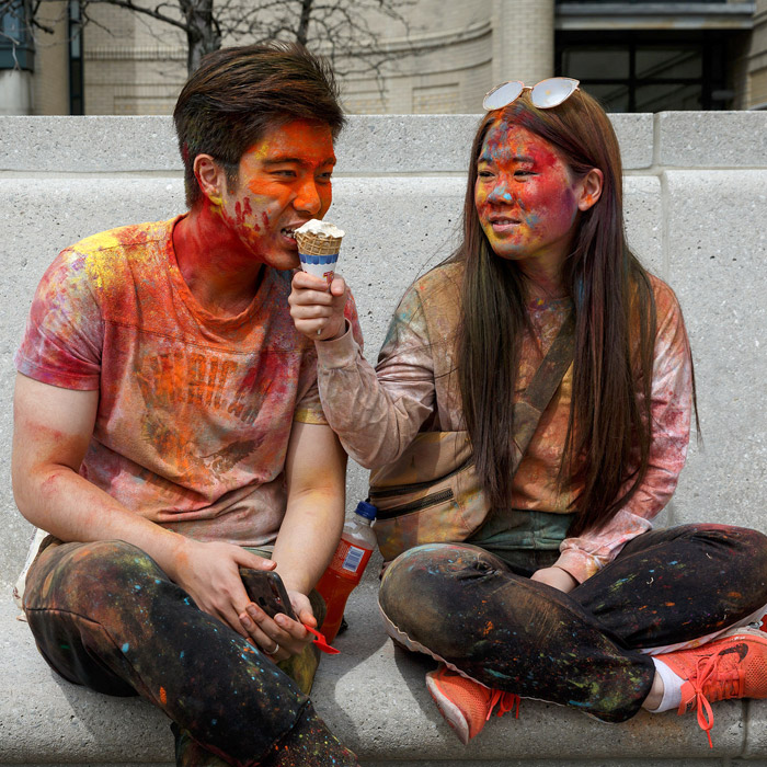 Students covered in colorful Holi festival dust eating an ice cream cone.