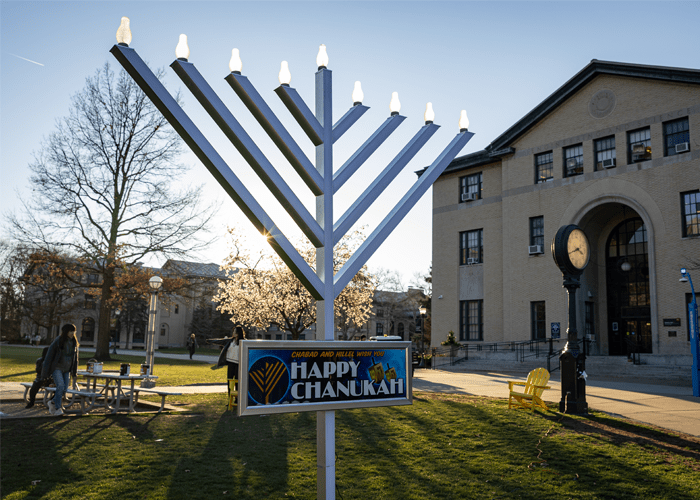 A human-sized menorah is lit on the Walkway with a sign that reads, "CHABAD AND HILLIL WISH YOU HAPPY CHANUKAH"