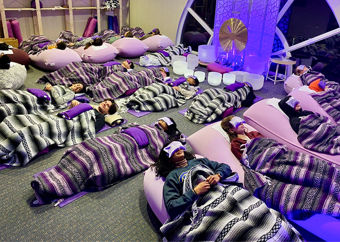Scottie Sound Bath session where students are lying on comfy blankets and pillows, surrounded by crystal bowls and bathed in purple light