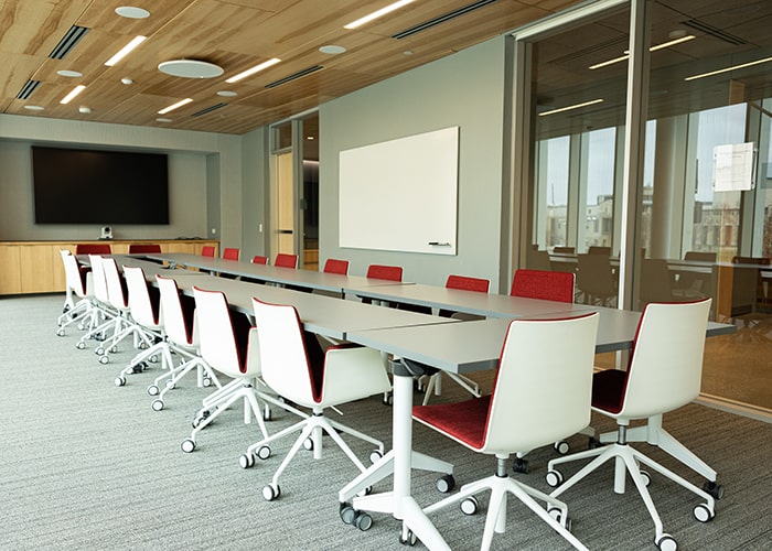 conference room with large table and many white and red chairs around it with a digital display and a whiteboard