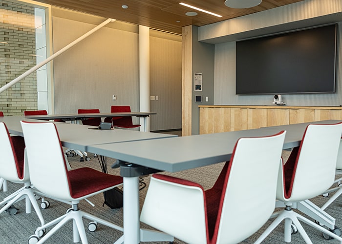 conference room with small table and several white and red chairs around it with a digital display