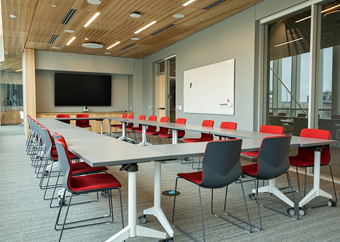 conference room with large table and many black and red chairs around it with a digital display and a whiteboard