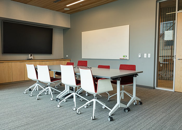 conference room with smaller conference table and several white and red chairs and a white board and digital display