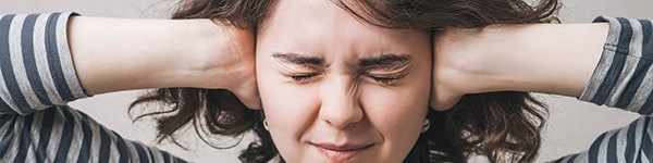 photo of woman tightly clasping her ears to block out sound and input