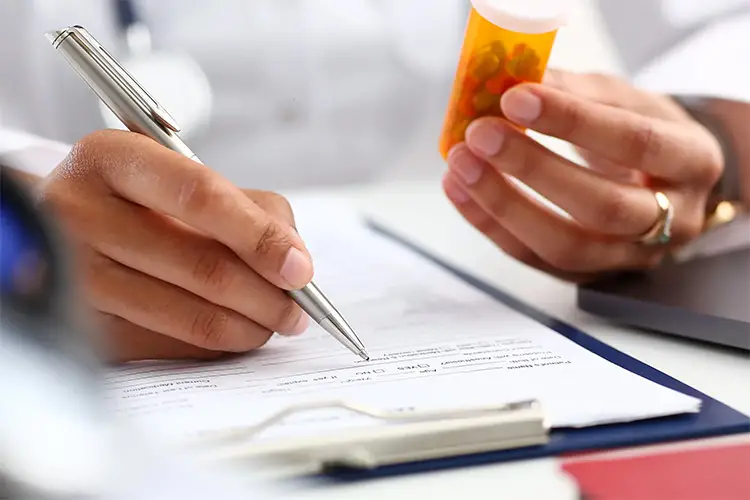 Photo of a doctor writing patient notes while holding a bottle of prescription medication.